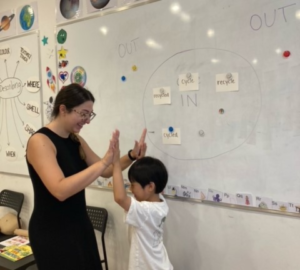 Speech pathologist gives high five to student in front of a white board of language exercises